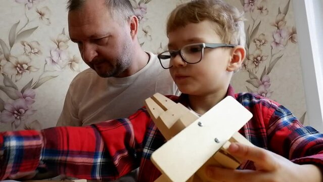 Happy father's day and childhood concept. Close-up of a father and a boy son in glasses work with hand tools, using a screwdriver, assembling a wooden house constructor at the table.