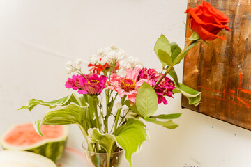 a bouquet with a rose in a vase on the shelf in front of the painting