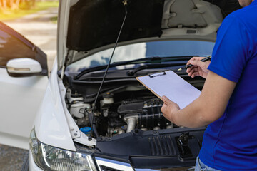 
The car insurer inspects the broken car. Male hand with clipboard with new car Worker checks clipboard insurance statement while mechanic inspects car at garage