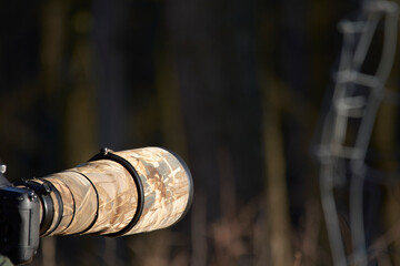 Camera with telephoto lens with camouflage cover and blurred background with space for text