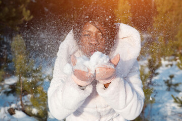 happy dark-skinned girl blows on frosty snow pile in hands falling and sparkling under bright sun...