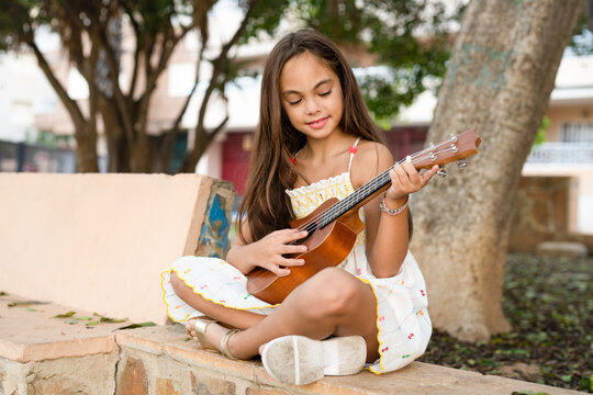 Pretty little girl playing the ukulele. The child plays music in a park outdoors.