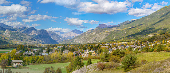 Fototapeta na wymiar Landscape in the middle of a large valley in the French southern alps. With a beautiful view of a small village and mountain ridges. Month of October with pretty fall colors.