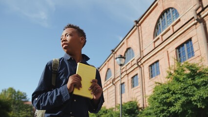 Low angle view of African-American teen boy with backpack lost in high school campus looking around