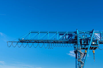 Part of an overhead crane with a cabin and hooks against the blue sky.