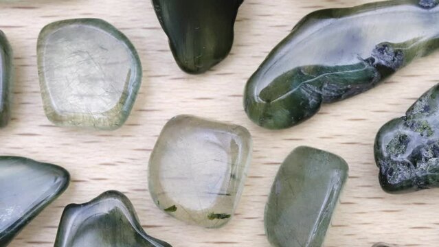 Green rutilated heap up jewel stones texture on light varnished wood background. Moving right seamless loop backdrop.