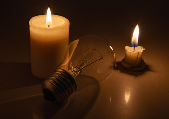 Switched off light or not glowing light bulb near a burning candles in total darkness during power...