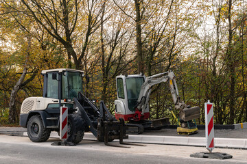 Small excavator and forklift stand on the side of the road at the construction site.