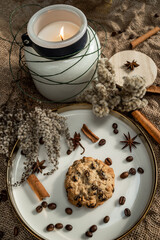 An elegant composition of candles, plates with a golden border, cookies and spices - anise, cinnamon and coffee. Against the background of burlap