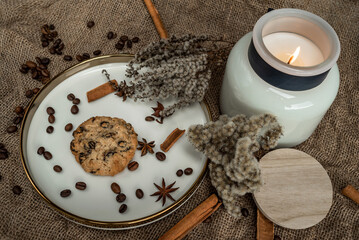 An elegant composition of candles, plates with a golden border, cookies and spices - anise, cinnamon and coffee. Against the background of burlap