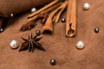 An elegant composition of spices - with anise, cinnamon on a suede brown background with beads and pearls