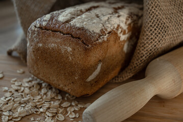 A loaf of bread on a bamboo board, sprinkled with oat flakes, in a burlap bag with garlands
