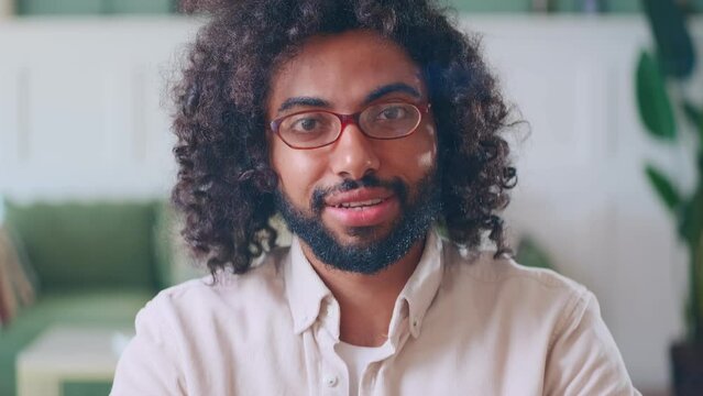 Young optimistic outgoing Arabian man with curly hair says hello and waving hand working in company advising clients via video call or customer service sits in home office. Headshot screen view