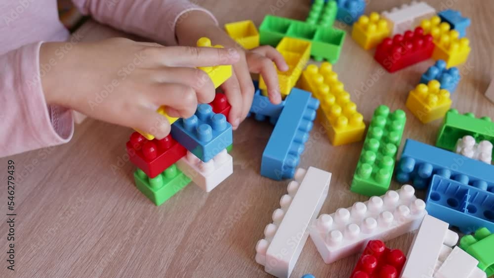 Poster Child builds a tower with a constructor from colored bricks blocks on the table, the concept of early development, fine motor skills of the hands