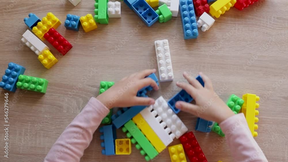 Poster child plays with a constructor from colored bricks blocks, top view