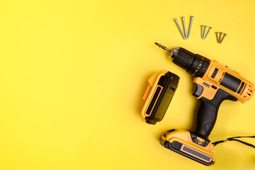 Cordless electric yellow screwdriver, battery and self-tapping screws on a yellow background. Copy space.