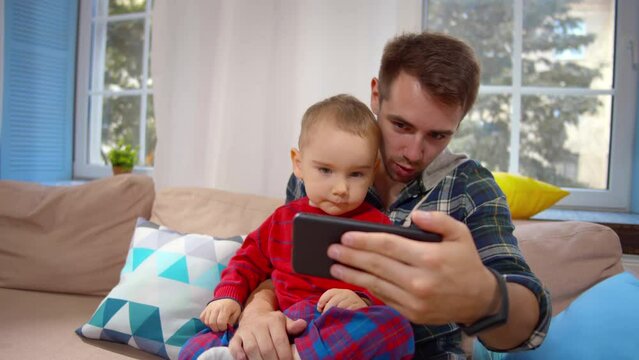 Happy father carrying his smiling son and making selfie or video in living room. Realtime