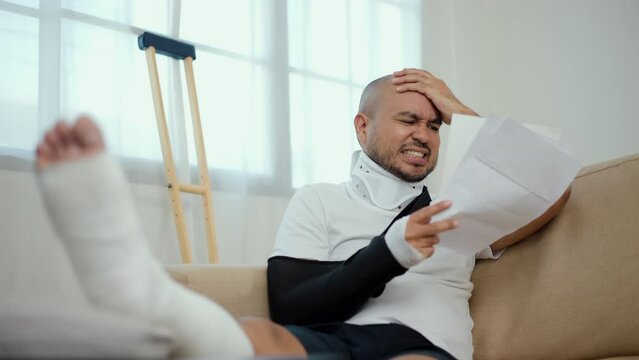 UnHappy man stressed pay invoice medical expenses from accident fracture broken bone injury with leg splints in cast, neck splints collar, sling support arm. Social security and health insurance.