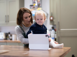 Fototapeta na wymiar Mother holding daughter drawing on digital tablet in kitchen