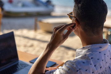 Man using laptop and earbuds at beach cafe