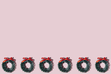 Christmas winter wreath with red ribbon bow and green pine on pink background. Wallpaper pattern frame. Top view flat lay.