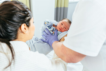Fototapeta premium Unrecognizable doctor giving newborn baby boy hispanic woman after birth in postnatal hospital.