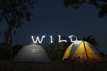 Camping in tent in the wilderness is an amazing adventure. Here two tents are pitched in front of a hill in full moon night.