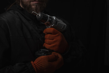 Hand holds cordless electric screwdriver with bit for screws and drilling isolated on black...