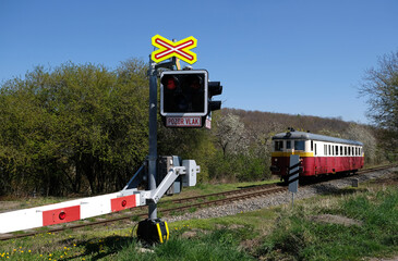The inscription in Czech - Attention train. Railroad crossing with closed barrier and passing train...