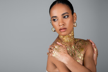 Stylish african american woman with golden foil on body touching shoulders isolated on grey.