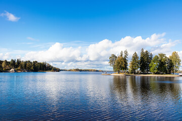 Autumn landscape, trees on lake shore under blue sky with white clouds
