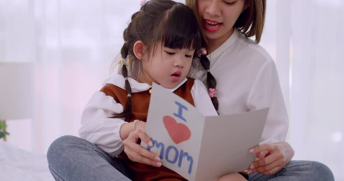 A little daughter giving mom handmade greeting card and wishing her Happy Mother's Day.