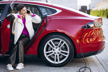 Woman charging electric car and talking on the phone