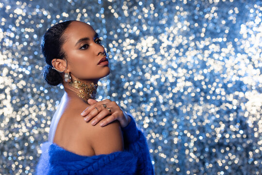 Young african american woman with foil on neck and accessories touching shoulder on sparkling background.
