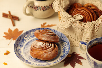 Tea party, break. Homemade cinnamon and raisin buns on vintage plates, a teapot and a wicker basket with buns in the background.