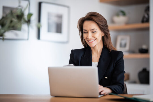 Happy woman sitting at table and using laptop while working from home