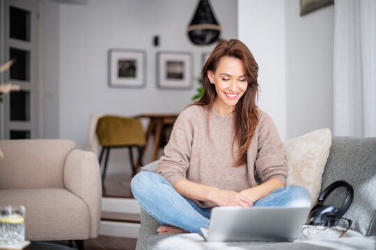 Smiling caucasian woman using laptop at home while sitting ont the sofa