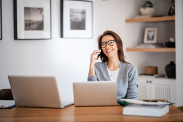 Fototapeta na wymiar Attractive woman wearing eyewear and casual clothes while working from home. Business woman using laptops and making a call. Home office.