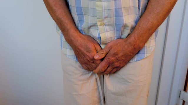 man in beige trousers, male hands on groin, mature man wants to go to toilet, senior 60 years old feels discomfort, concept of men's health, age-related urinary incontinence