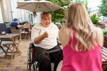 Fototapeta na wymiar Mother with disability in wheelchair talking to her daughter while sitting at the table in cafe