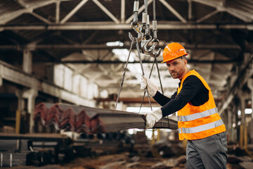 Man working at steel factory with a crane lifting steel pipes