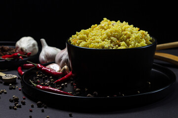 Yellow pilaf in a black plate on a black background. Traditional oriental dish