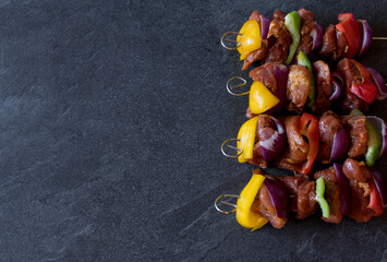 Shashlik skewers with red, green and yellow bell peppers, red onions and marinated pork tenderloin isolated on dark background