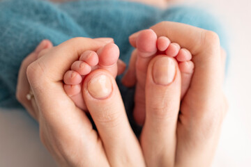 Mother is doing massage on her baby foot. Close up baby feet in mother hands on a blue background. Prevention of flat feet, development, muscle tone, dysplasia. Family, love, care, and health concept