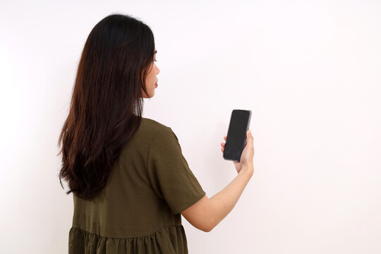 Back view of young woman standing holding a cell phone. Isolated on white background