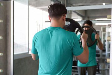 Back view of athletic male exercise with barbell weight plate in the sport gym