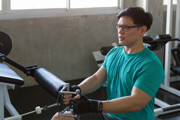 Asian young man pulling weights in seated cable row machine in the sport gym. Athlete male exercise with rowing machine in the gym