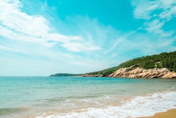 Seawaves washing the sandy beach with a rocky cliff and vegetation in the background