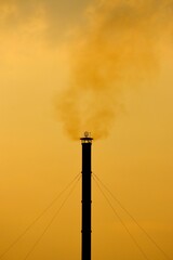 Vertical of factory pipe emitting black toxic smoke in the air with a yellow sky in the background
