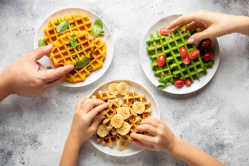 Happy family having breakfast. Parents with child eating variety Belgian waffles. cropped image,...